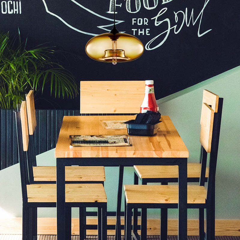 Amber glass pendant above a wooden table with Black-framed wooden chairs, menus, napkins, bottle and a plant