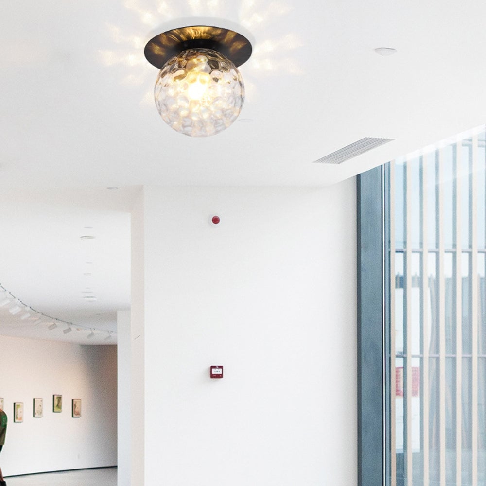 Clear textured glass globe beneath a dark ceiling plate in a bright corridor