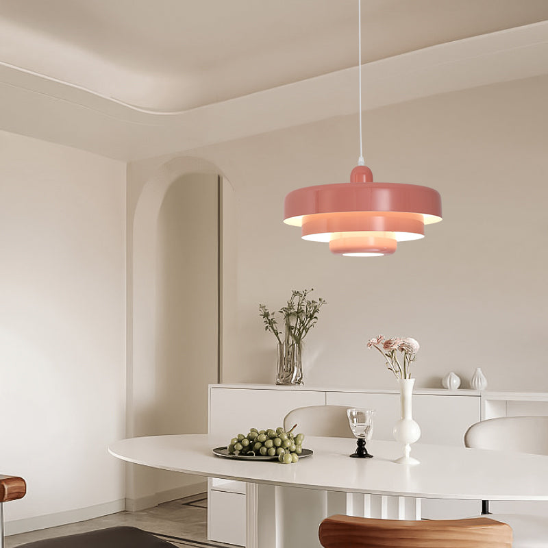Pink three-tier pendant light above a white table with grapes, a glass and a vase