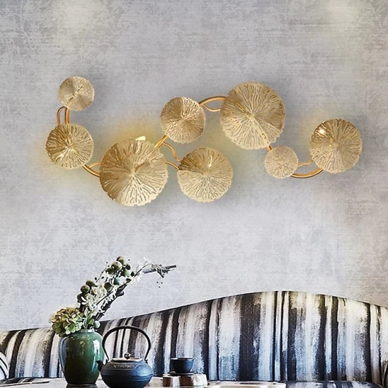 Horizontal eight-leaf gold-colour wall light above a striped sofa and a table with tea accessories
