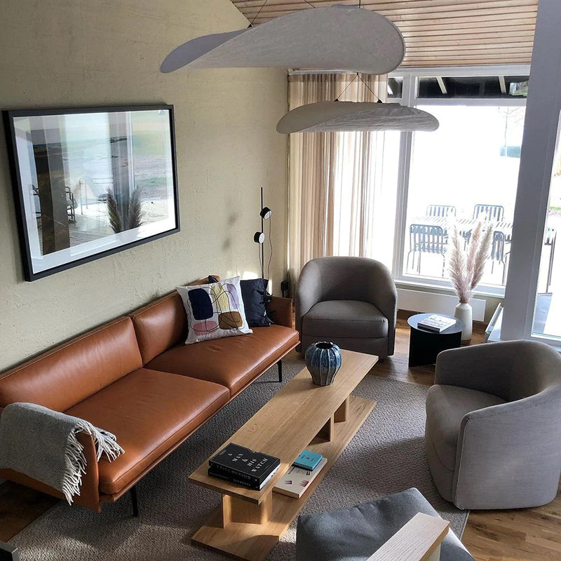 Two curved white pendants above a living room with a brown leather sofa and gray armchairs