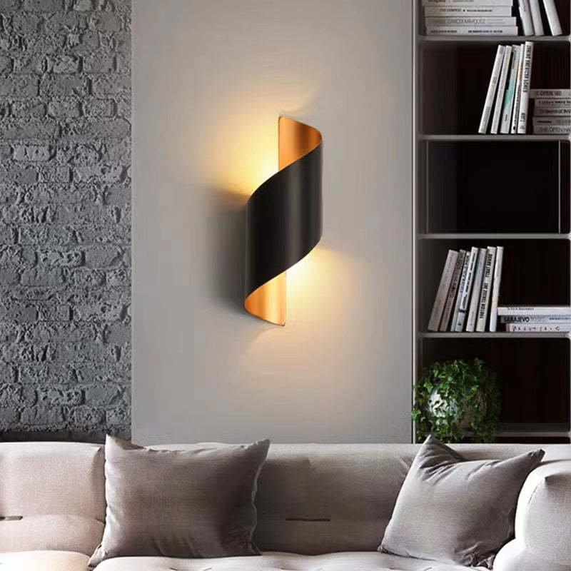 Black and gold wrap wall light above a pale grey sofa beside a bookcase and rough textured wall