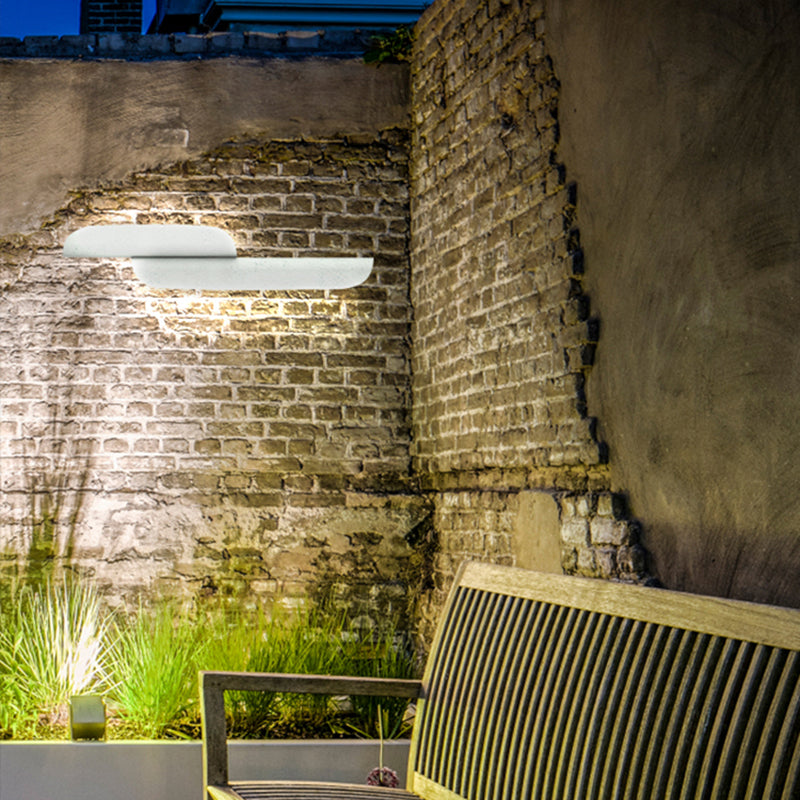 Two white curved wall lights in opposite orientations on a brick courtyard wall above a bench