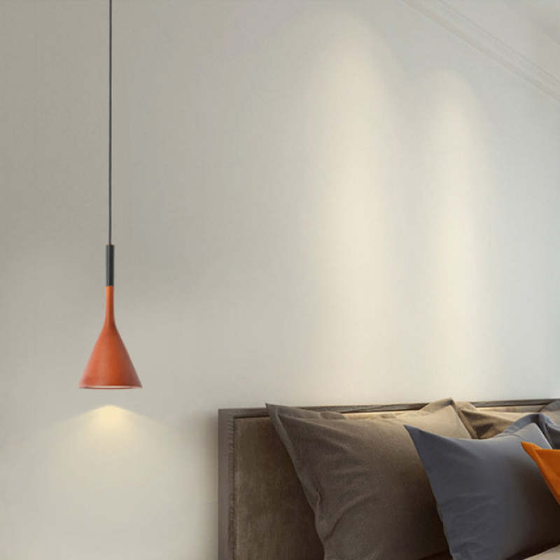 Red cone pendant beside a wooden headboard with grey and blue pillows, casting light onto the wall