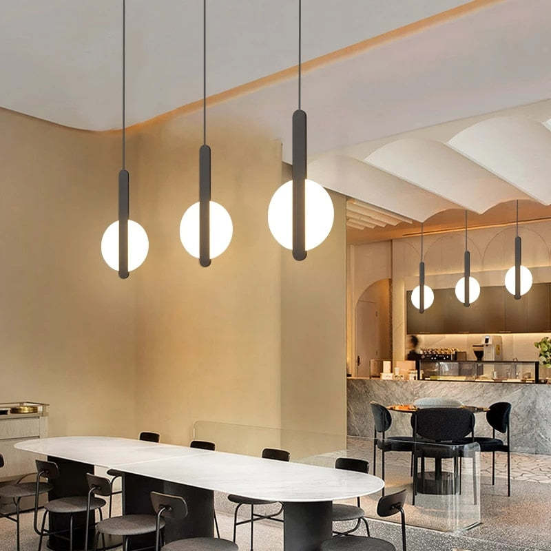 Black vertical-bar and luminous-disc pendants arranged above a dining table with a mirrored wall