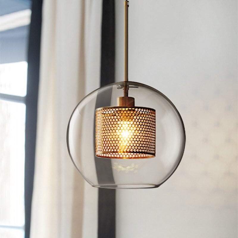Gold Oneal C round glass pendant with a glowing perforated cylindrical insert beside a window