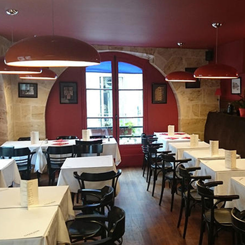 Wine-red dome pendants above separate restaurant tables with white cloths near a stone archway