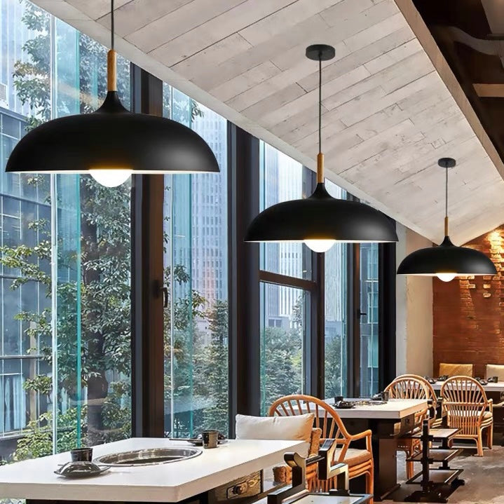 Three black shallow dome pendants on separate round canopies above restaurant tables beside tall windows