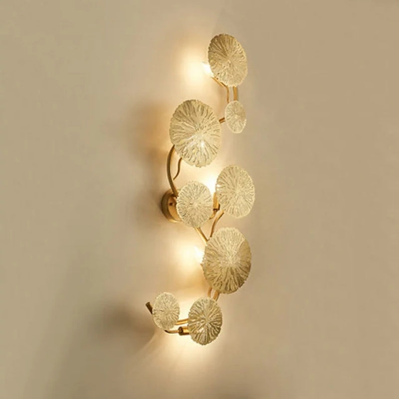 Vertical eight-leaf gold-tone wall light with a round plate and light behind the textured discs