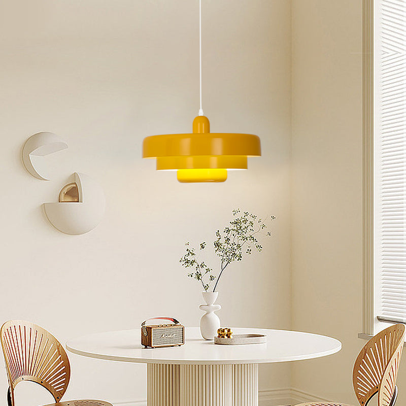 Yellow layered pendant light above a white round table with a radio and vase beside window blinds