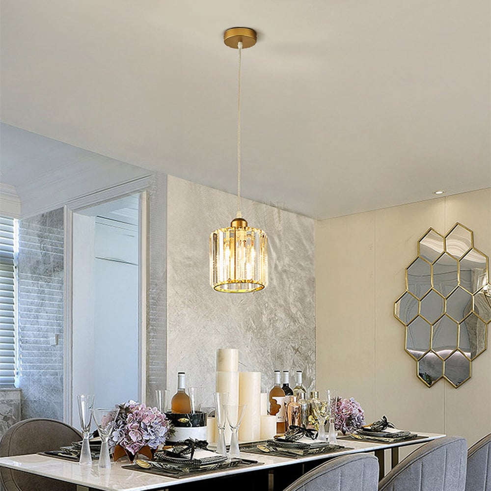 Single gold cylindrical glass pendant above set dining table with white candles, bottles and hexagonal wall mirror