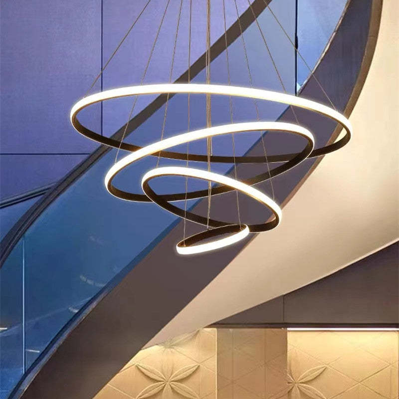 Four-ring pendant light with Brown-toned metallic frames and White illuminated outer bands beneath a staircase and glass panels
