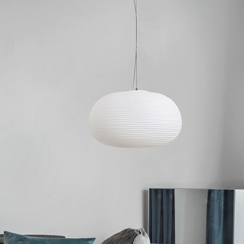 Unlit wide oval ribbed white shade hanging above a cushioned seat and reflective panel