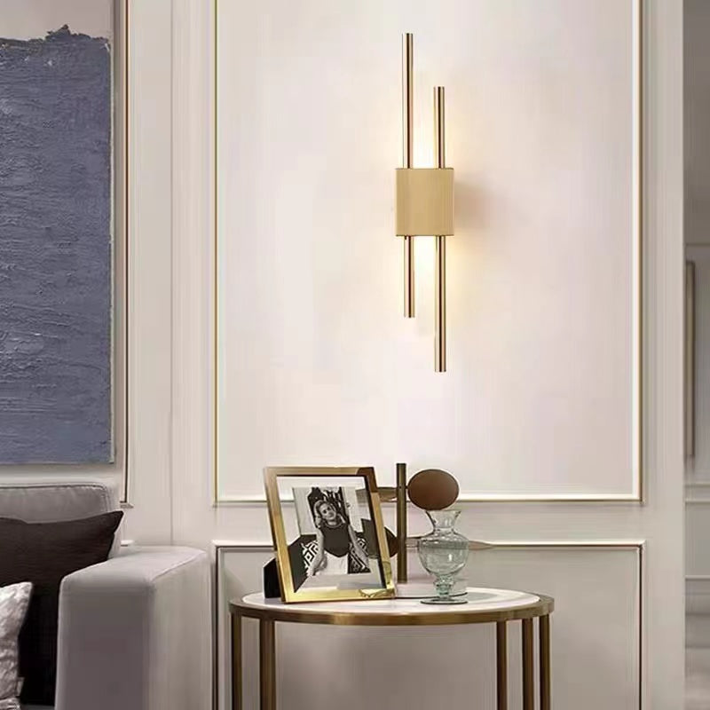 Gold-coloured Alana wall light with staggered rods and a lit bar above glass ornaments on a round side table