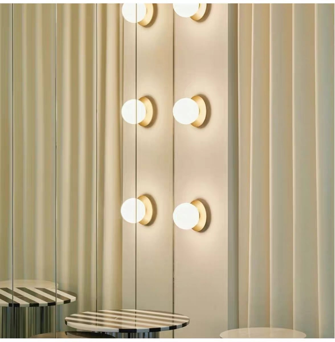 White glass globes on gold-tone plates arranged vertically beside a mirrored wall