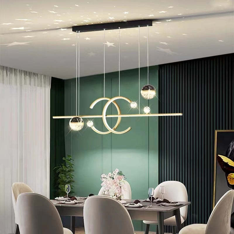 Lit gold-tone Madina Double-C pendant above a dining table beside a green wall, with stars pictured on the ceiling