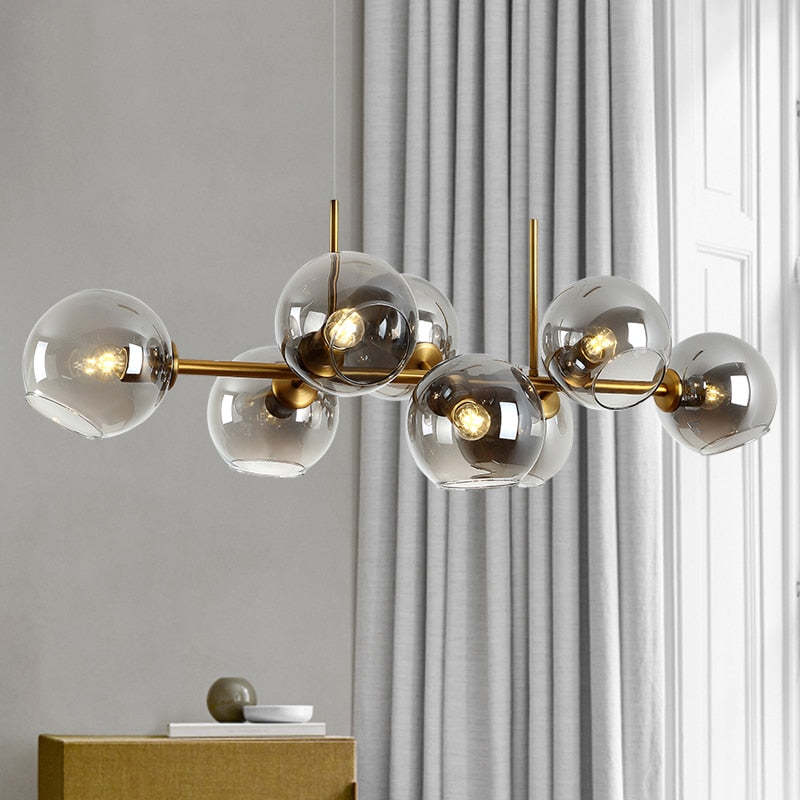 Gold body and smoke-gray glass pendant with glowing bulbs beside grey curtains, window and cabinet