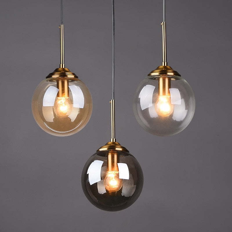 Three globe pendant lights with gold-tone stems against a grey background