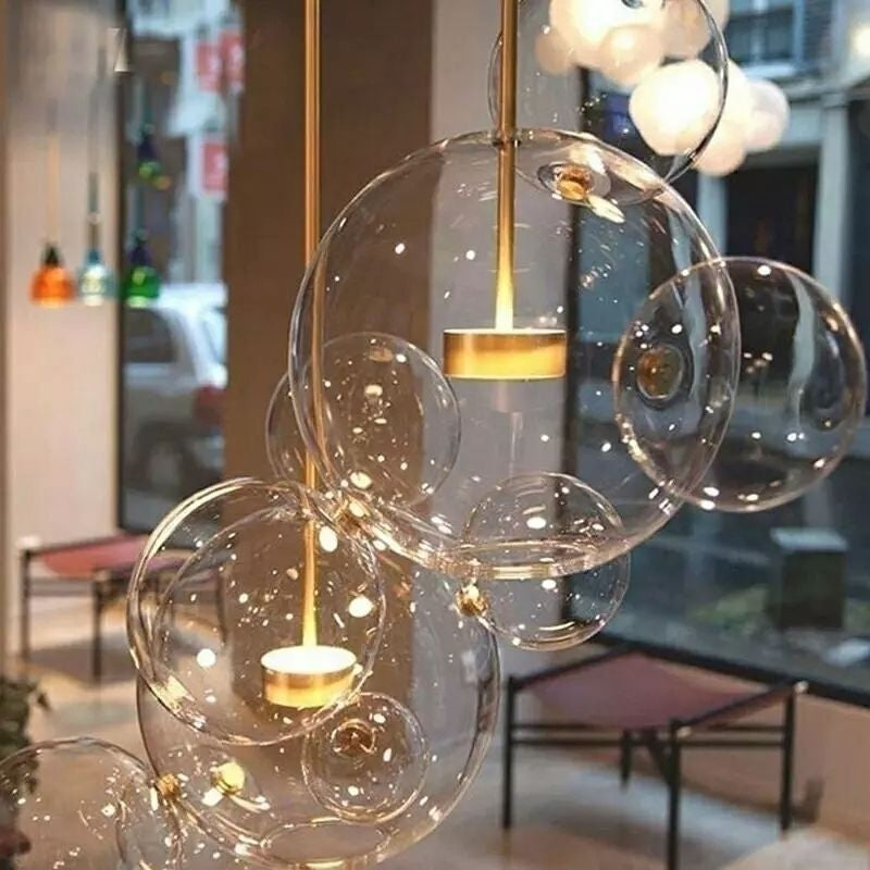 Showroom close-up of several clear bubble pendants, gold stems and central housings, with seating and other lights behind