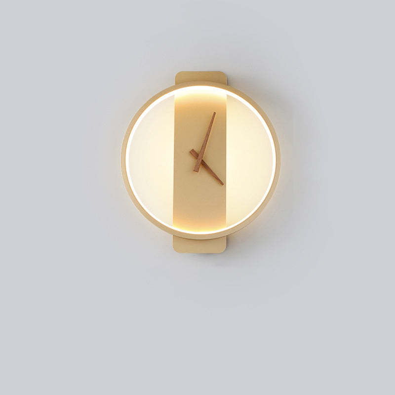 Gold round wall light with warm-looking inner illumination, vertical backplate and Brown hands against a Gray wall