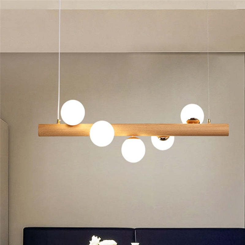 Light wooden bar pendant with five White globes above a cropped Dark banquette against a Gray wall
