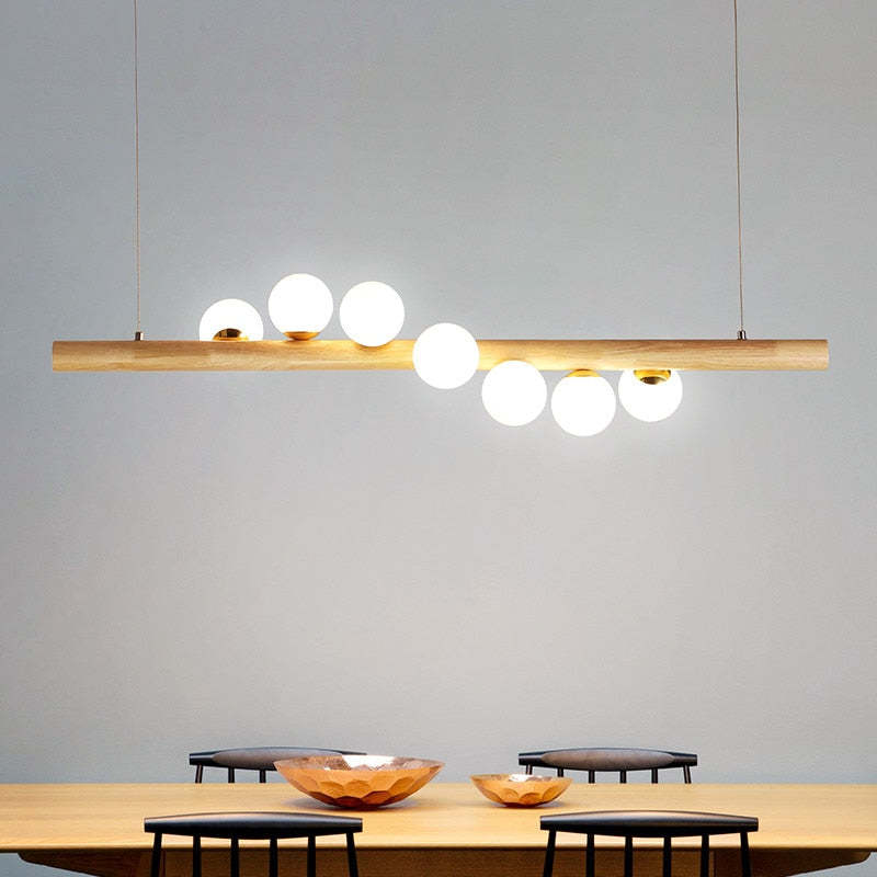 Light wood seven-globe pendant above a wooden table with Black chairs and wooden bowls against a Gray wall