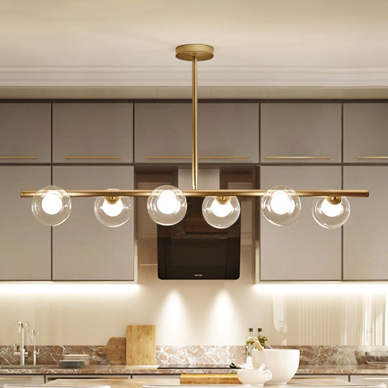 Gold six-globe linear pendant with central straight stem and round canopy above a kitchen island