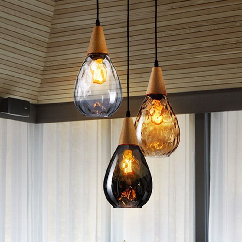 Cluster of clear, amber and smoke-gray Avi pendants with wood tops below wood-slat ceiling beside curtains