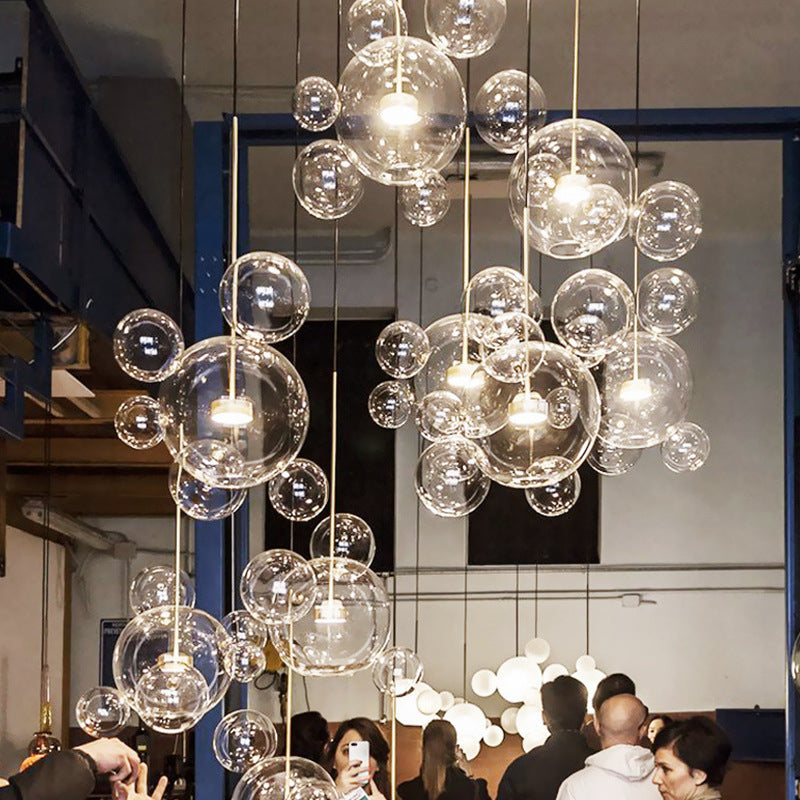 Showroom display of many clear bubble pendants at different heights, with people below and other white globe lights behind