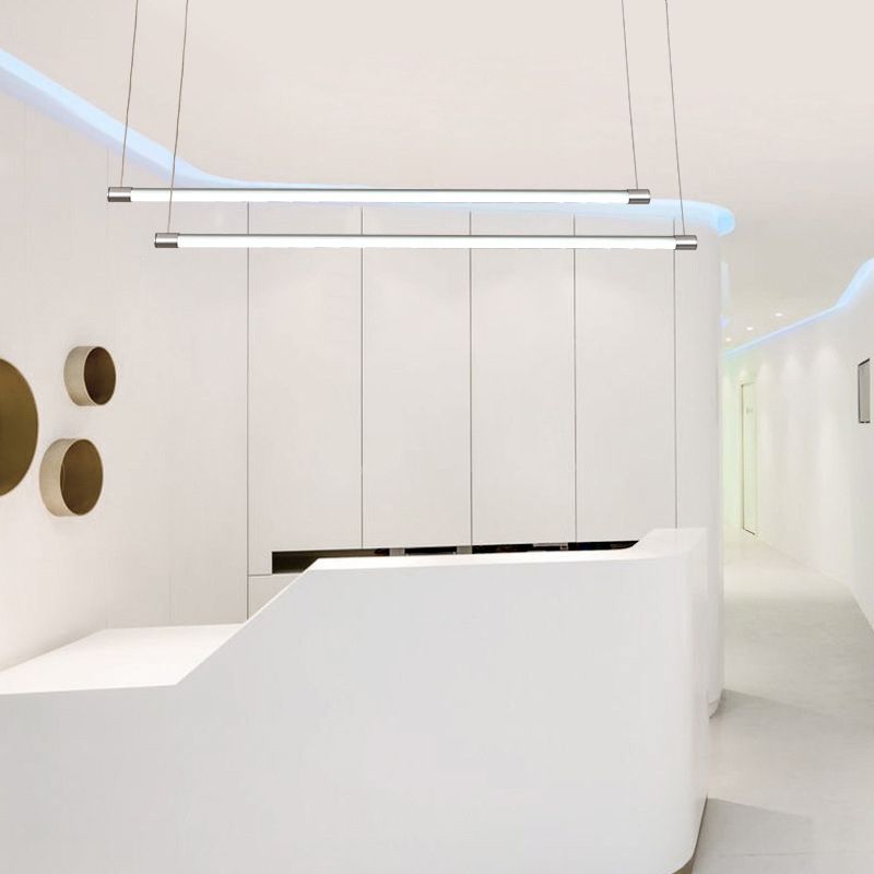 Two silver-endcap linear pendants above a white reception counter with round wall recesses