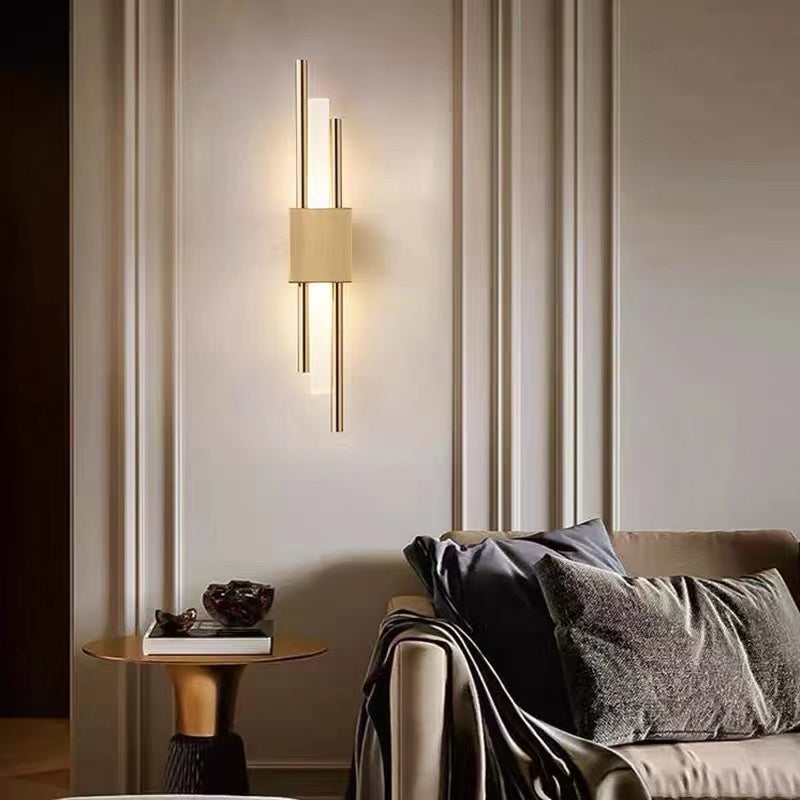 Gold Alana wall light above a small table beside a sofa, with warm wallwash and staggered vertical rods