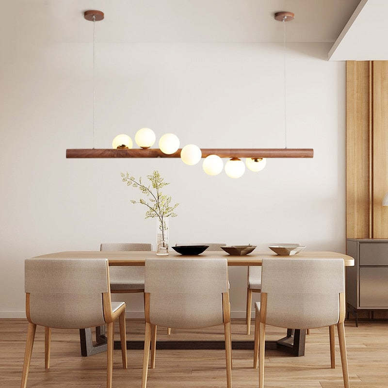 Dark wood seven-globe pendant above a dining table with Cream chairs, bowls and a branch vase beside curtains