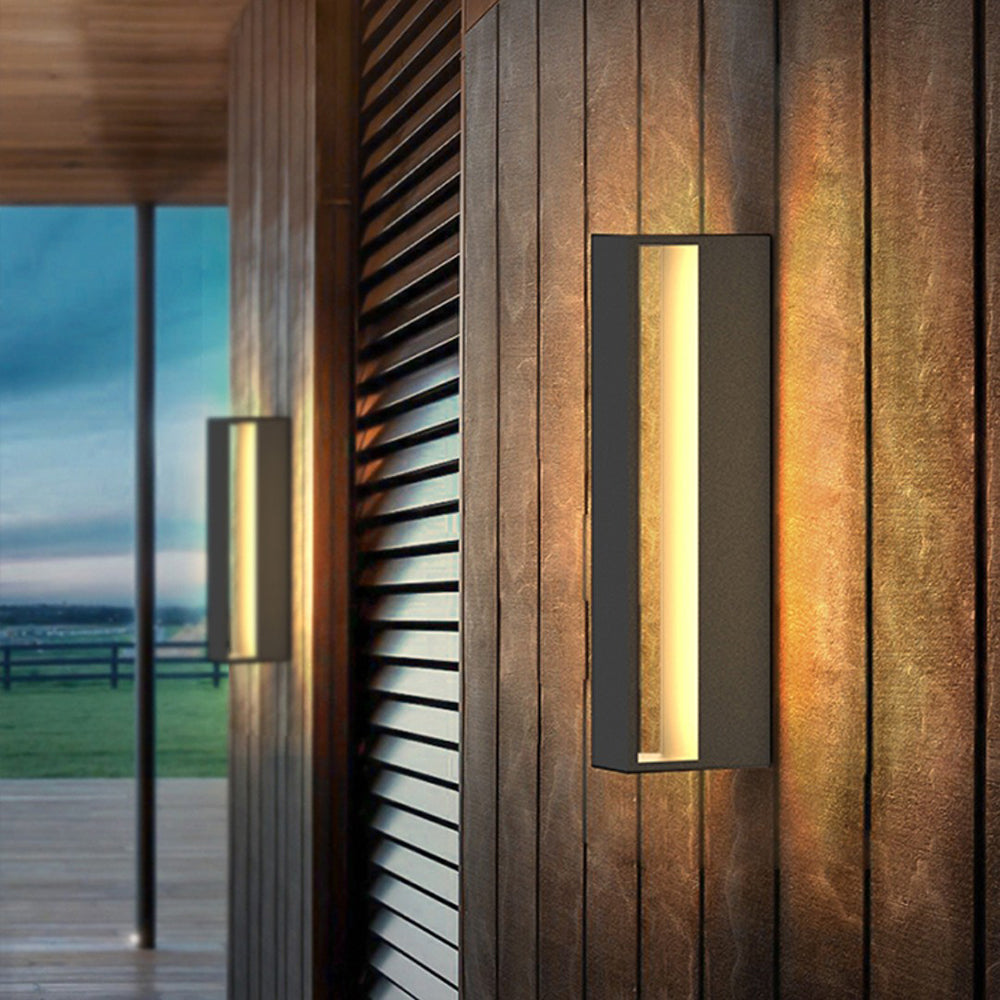 Black open-frame wall light glowing on wooden cladding beside louvres and a glazed door