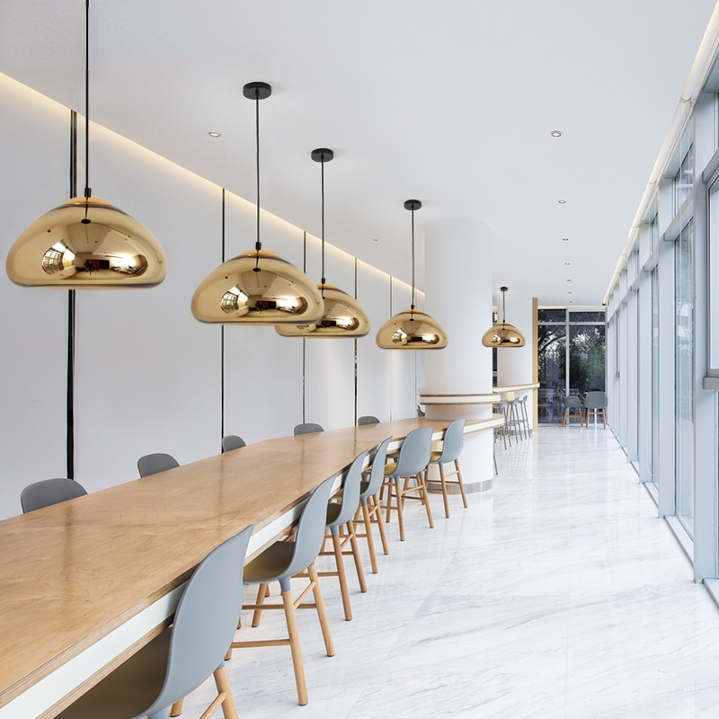 Gold reflective dome pendants in a row above a long dining table
