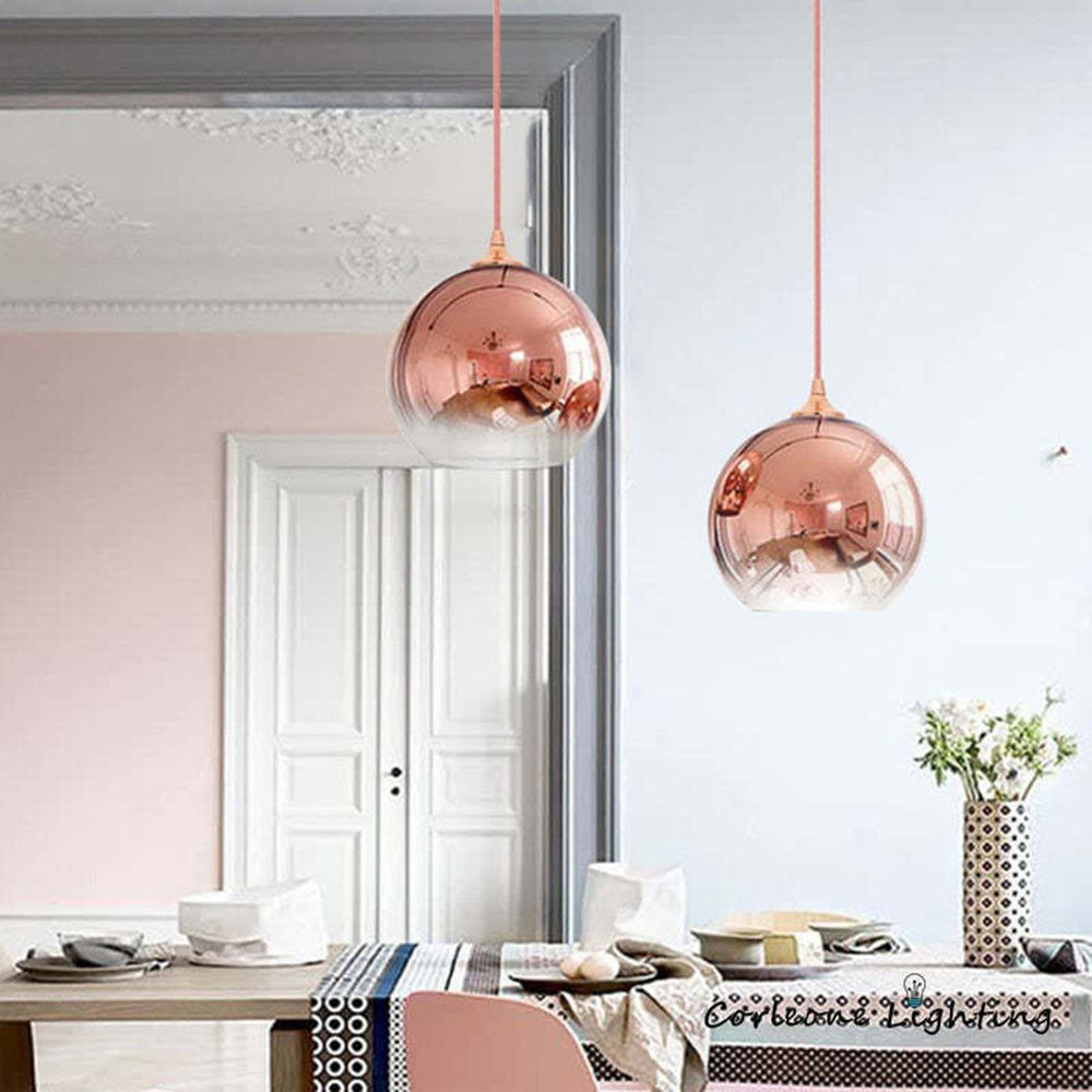 Two rose-gold globe pendants above a dining table beside a mirror