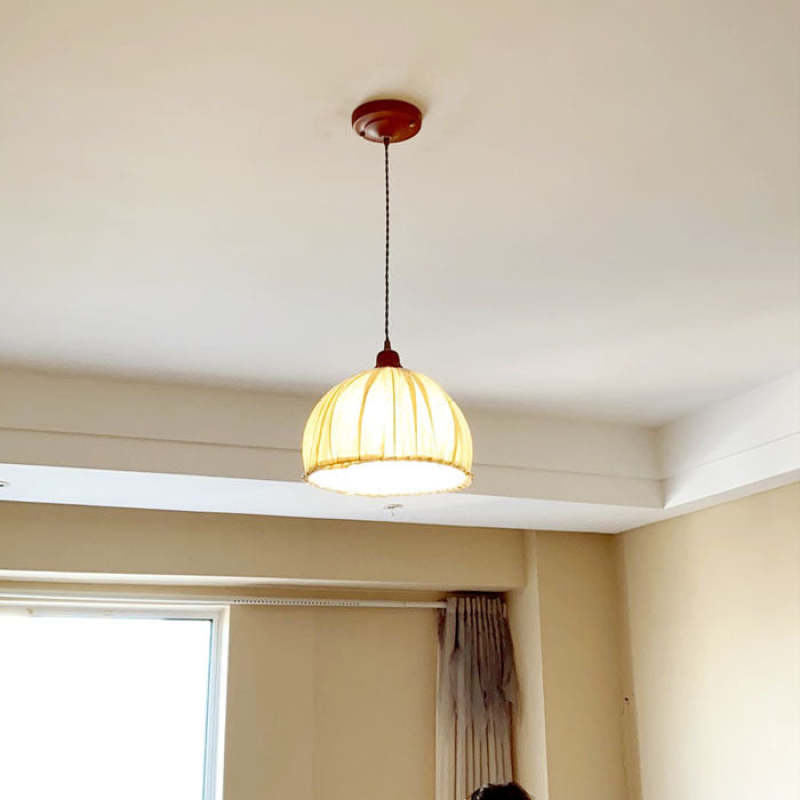 Illuminated beige fabric pendant on a long wire beneath a round ceiling canopy in a room with a window
