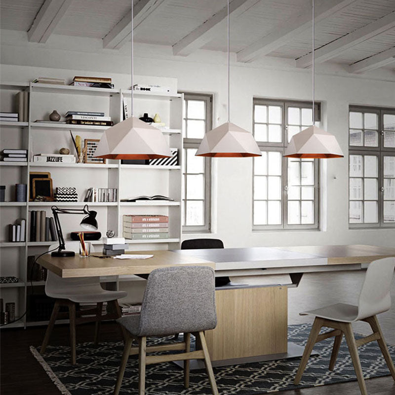 Three white faceted pendants with copper-toned interiors above a long worktable beside windows
