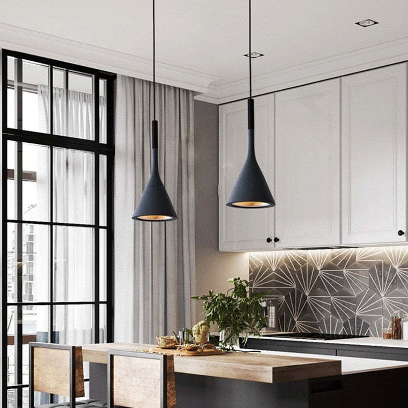 Two dark cone pendants above a wooden breakfast table beside white kitchen cabinets and a patterned backsplash