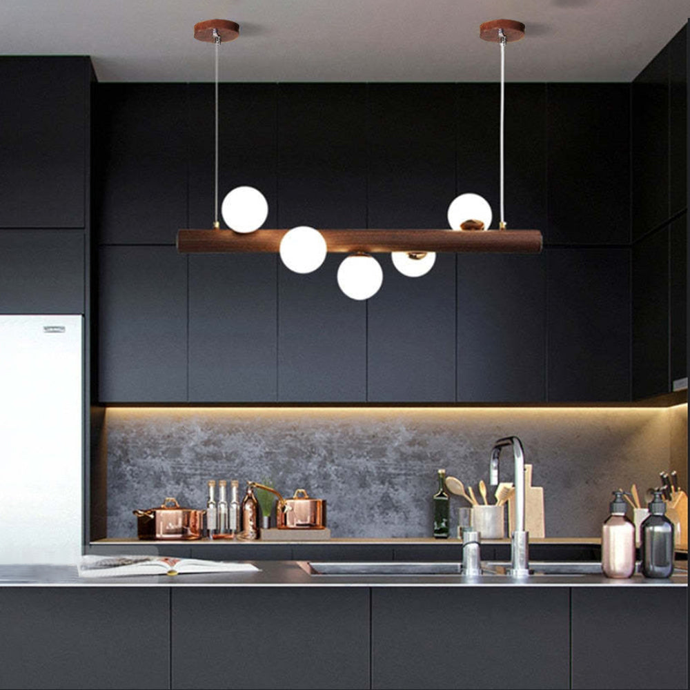 Dark wood five-globe pendant above a kitchen island with a sink and tap, Dark cabinets, pots and a White jug