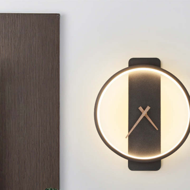 Cropped Black round clock-face wall light with warm-looking inner illumination beside a Dark wood panel