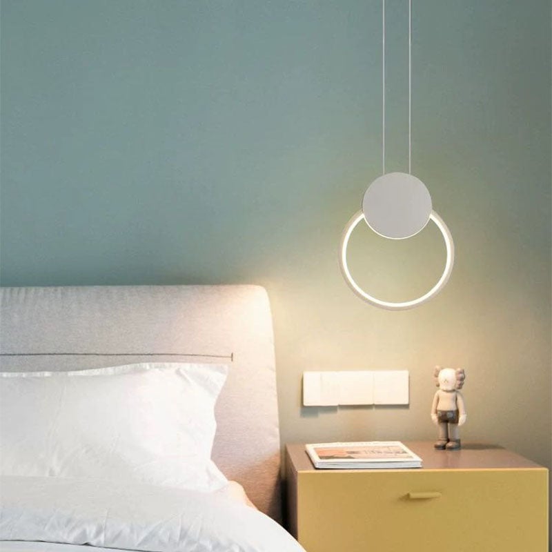 White circular loop pendant with a round top cover beside a bed and gold-coloured cabinet