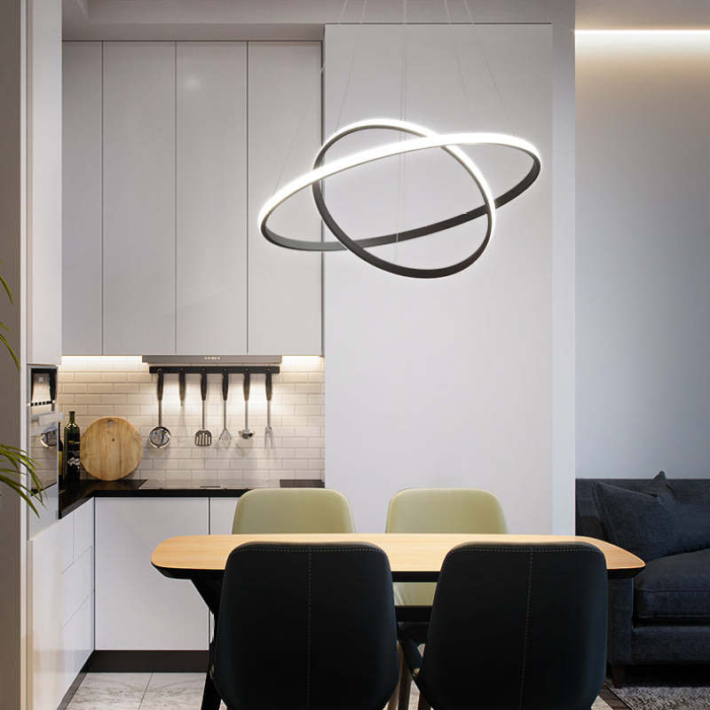 Black crossed two-ring pendant light above a wooden table with Green and Black chairs beside a White kitchen