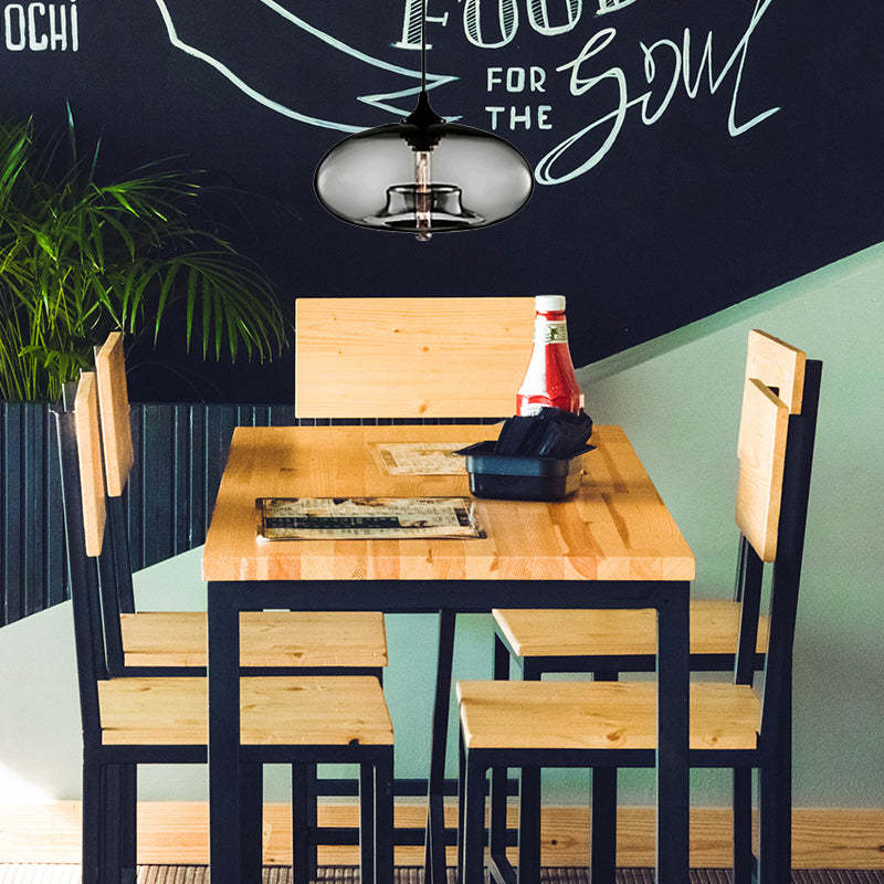 Smoke Gray oval glass pendant light above a wooden dining table with Black chairs, bottle, menus and a plant