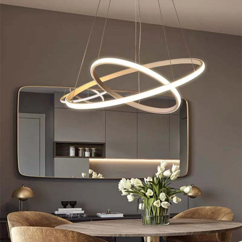 Gold-toned crossed two-ring pendant light above a dining table with White flowers, wall mirror and Gold dome table lamps