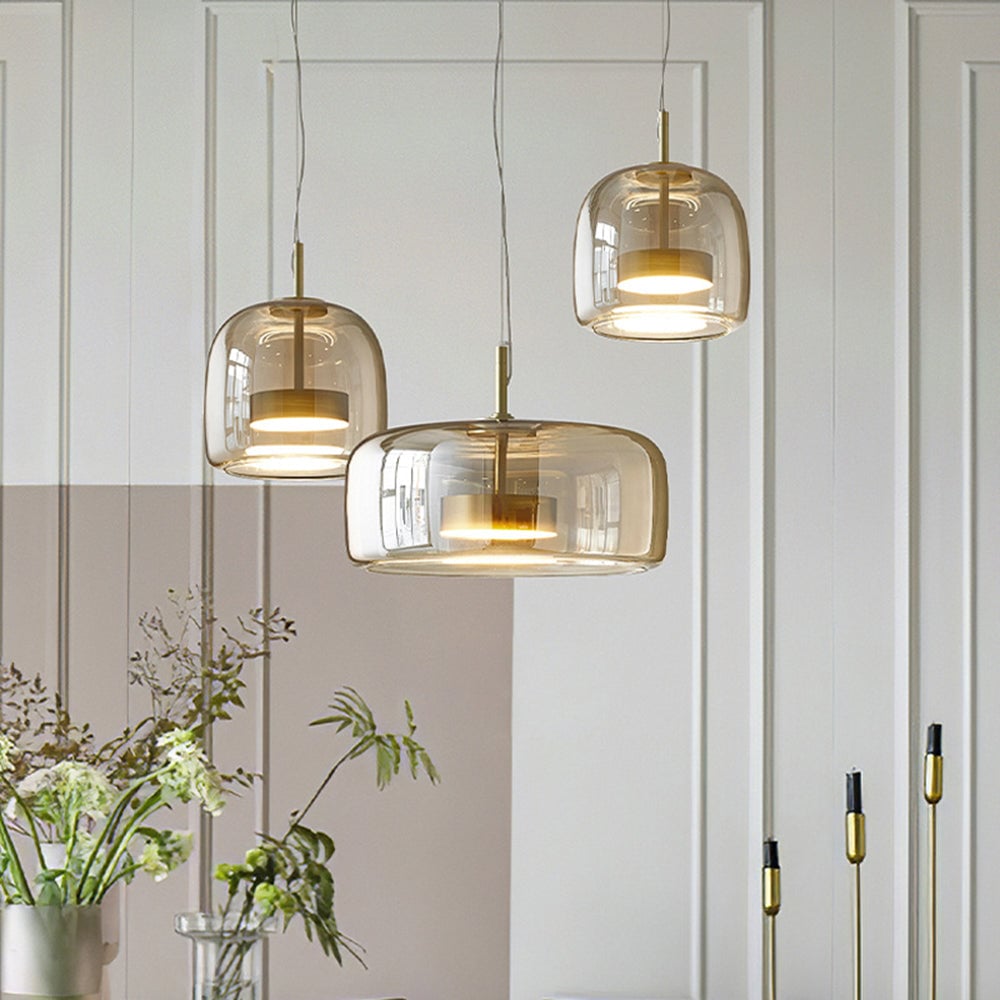 Three clear Hailie glass pendants with gold-tone inner housings at staggered heights above vases against paneled wall