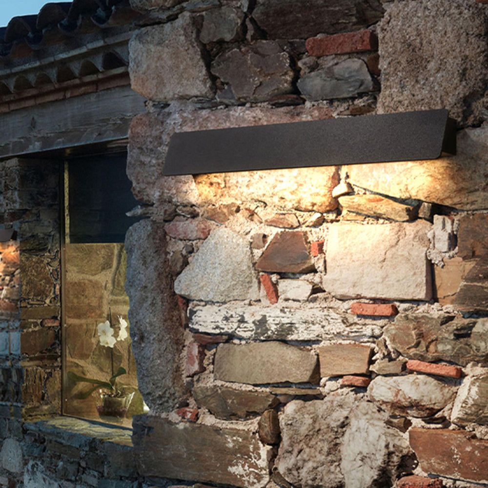 Black Orr linear wall light illuminating a stone wall from above