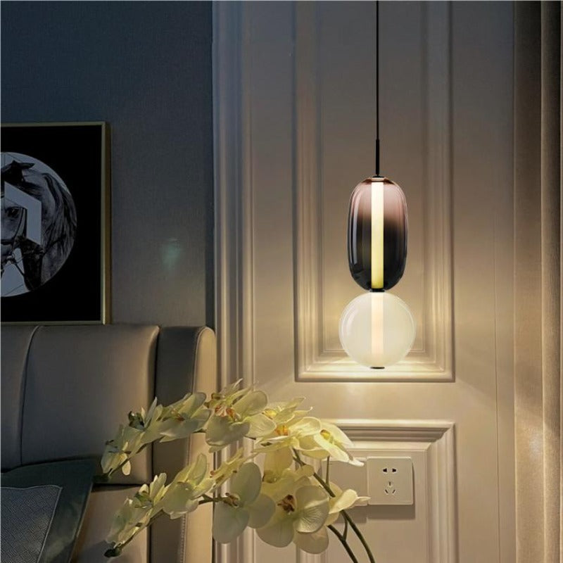Smoked and pale two-form glass pendant beside a bedhead, panelled wall, framed art and white orchids