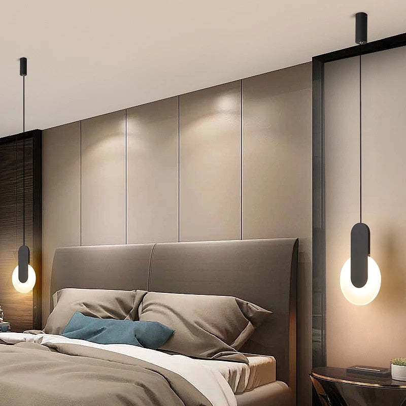 Two black short-bar and circular-disc pendants hanging beside a bed and upholstered headboard