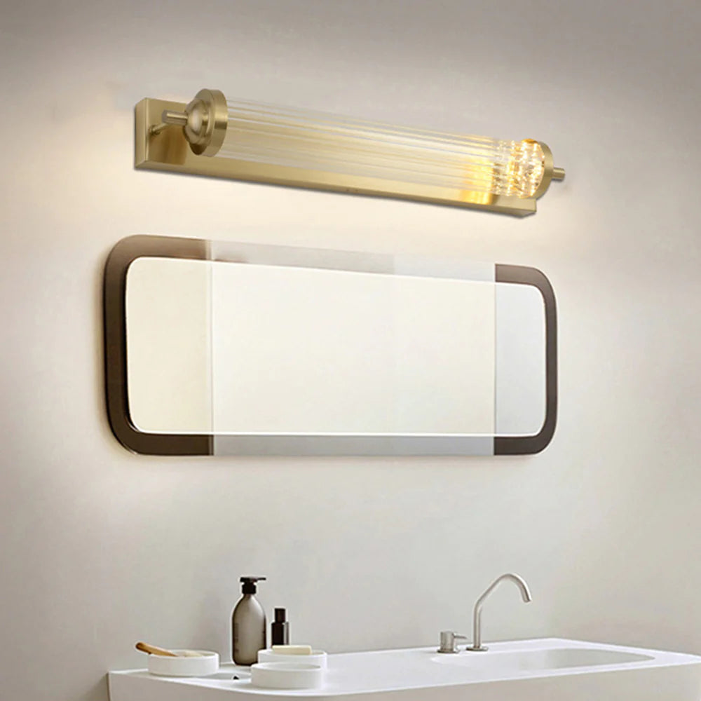 Gold cylindrical wall lamp above an oval-cornered mirror and white basin.