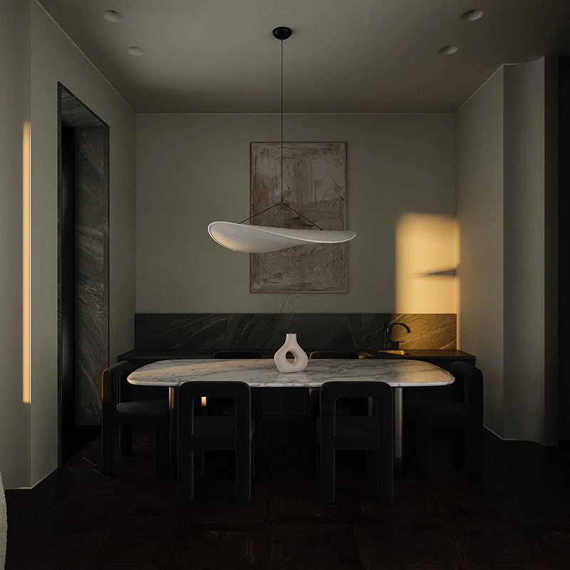 Unlit curved white pendant above a dining table in a dark interior with a white sculptural vase